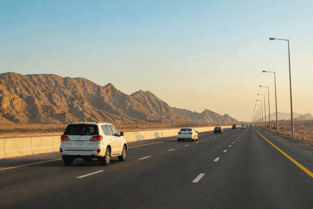 Cars driving along a smooth highway toward Ras Al Khaimah with desert mountains in the background, representing a long-distance Dubai to Ras Al Khaimah car lift journey